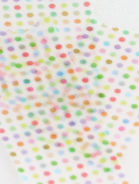 A close-up of a white surface covered with many small multicolored polka dots in pastel and bright shades.