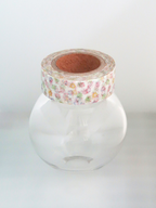 A roll of floral washi tape wrapped around the neck of a clear glass jar, set against a plain white background.