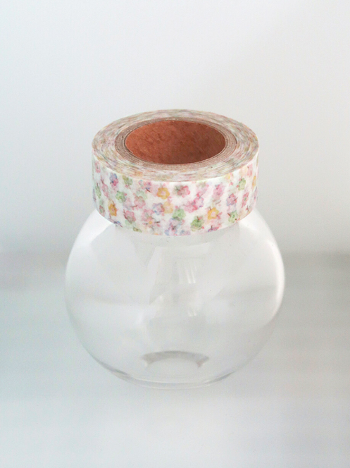 A roll of floral washi tape wrapped around the neck of a clear glass jar, set against a plain white background.