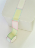 A roll of pastel washi tape with alternating soft blocks of pink, yellow, green, and white, shown unrolled over a white surface.