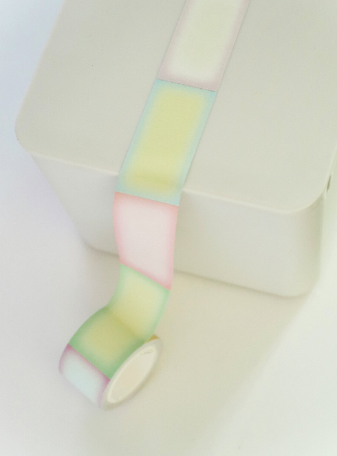 A roll of pastel washi tape with alternating soft blocks of pink, yellow, green, and white, shown unrolled over a white surface.