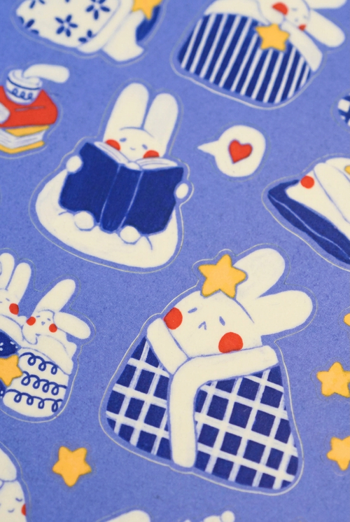 Close-up of reading and blanket-wrapped bunny stickers with yellow stars on purple backing.